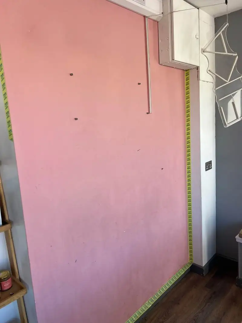 Scuffed pink feature wall masked with tape and the sign taken down, ready for repainting