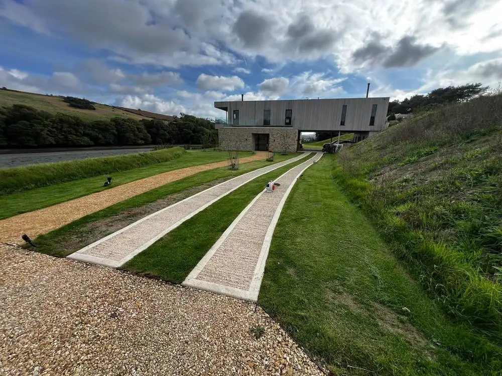 Mown grass strips and verges along the driveway of a modern house beside the estuary
