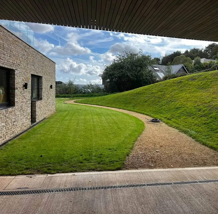 Neatly cut lawn, curved gravel path and grassed bank beside a stone house