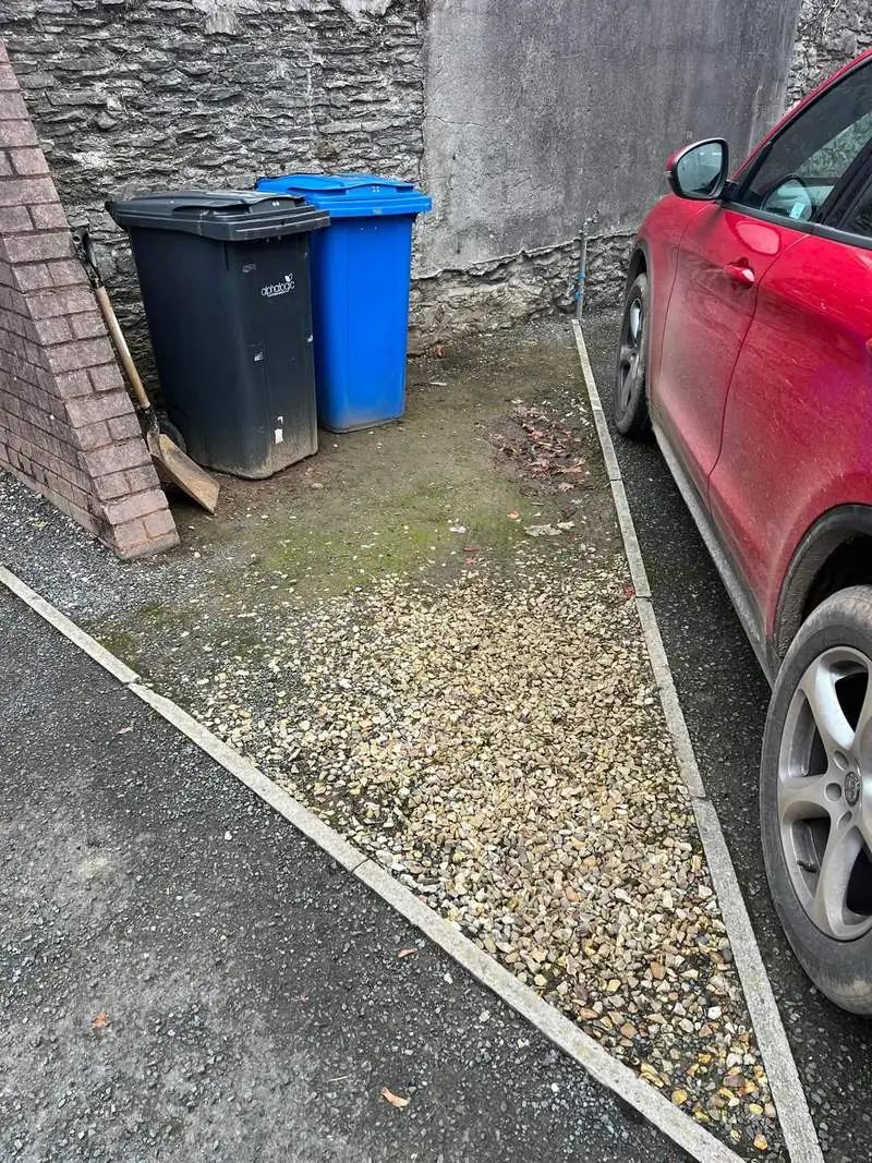 Gravel parking area before the work, thin, mossy and patchy, with bins stood on it